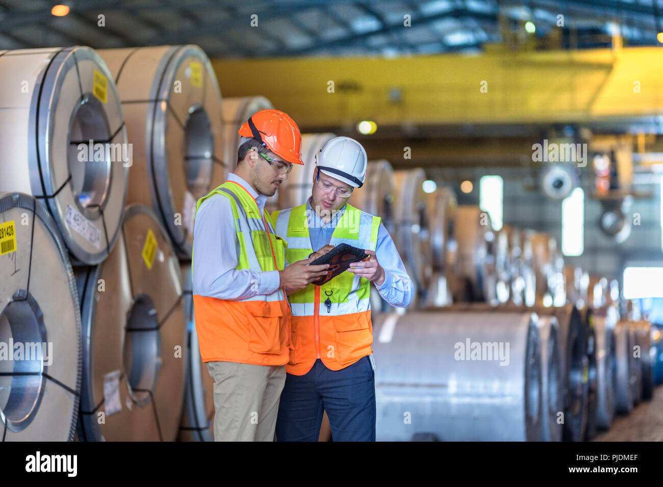 Los trabajadores mediante tableta digital por filas de chapa de acero en el almacenamiento en el puerto Foto de stock
