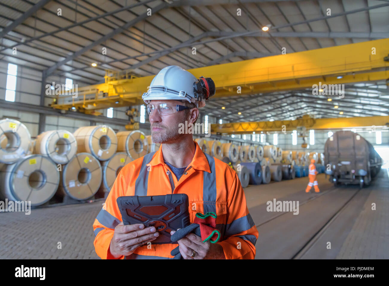 Trabajador con digital comprimido por filas de hoja de acero en el almacenamiento en el puerto Foto de stock