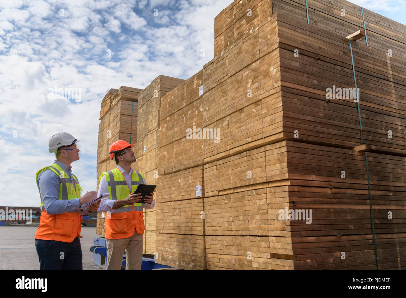 Los trabajadores con pilas de madera en el almacenamiento en el puerto Foto de stock