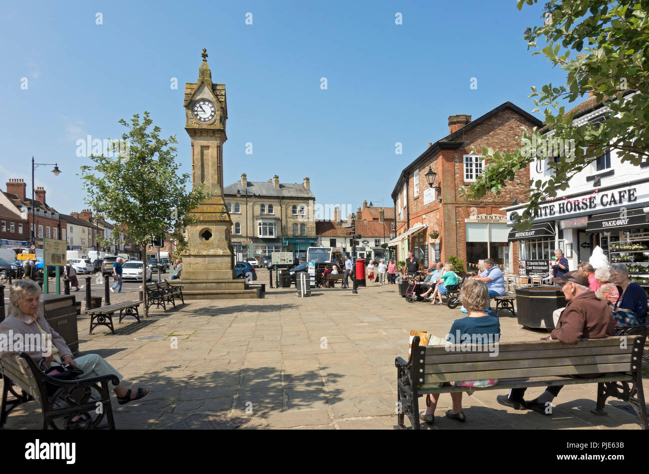 Gente compradores relajarse sentados fuera en el centro de la ciudad en verano Market Place Thirsk North Yorkshire Inglaterra Reino Unido GB Gran Bretaña Foto de stock