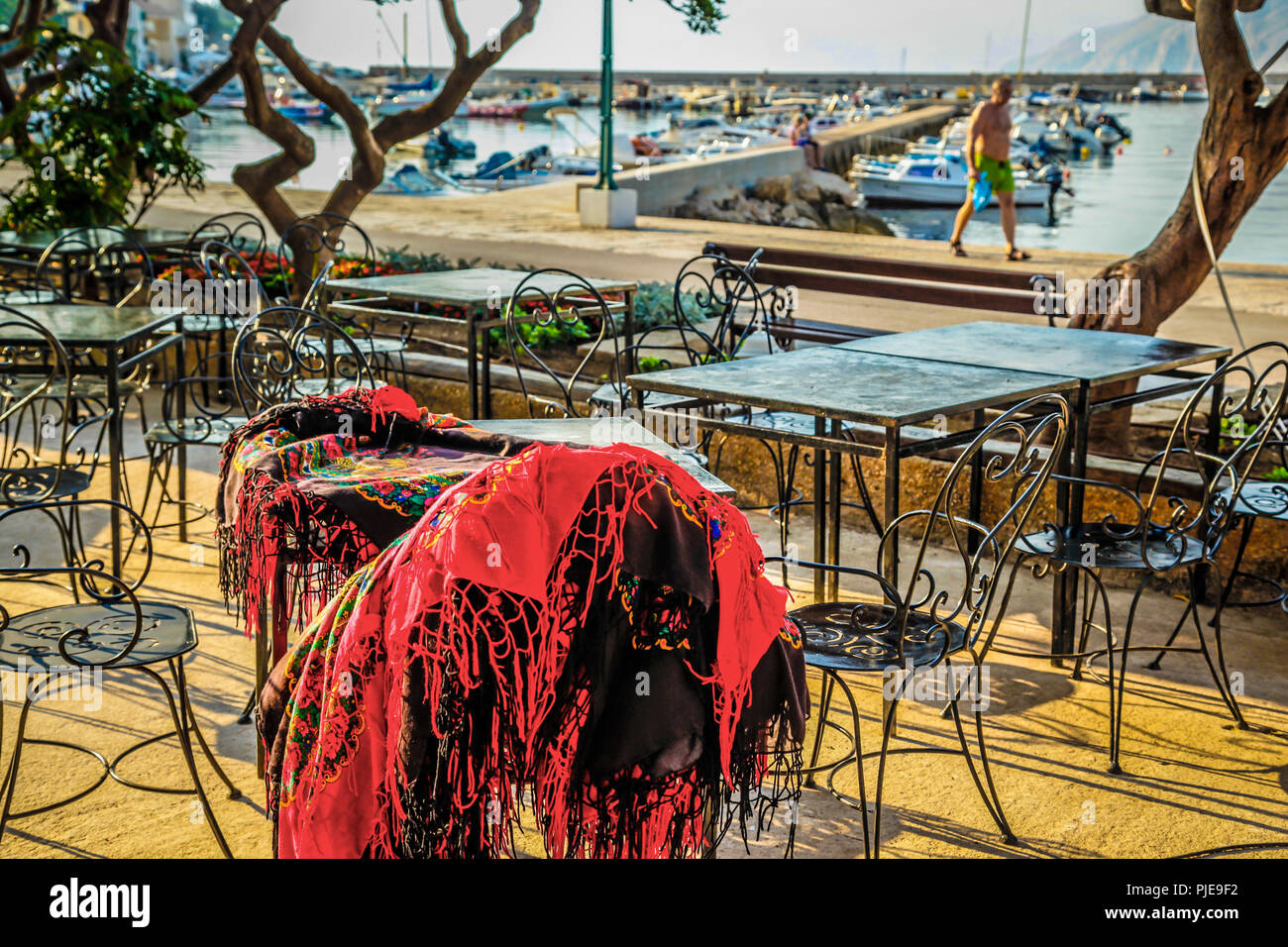 Un chal proveedor deja sus bufandas en una mesa vacía en un café con vistas  al puerto en Baska en la isla croata de Krk Fotografía de stock - Alamy