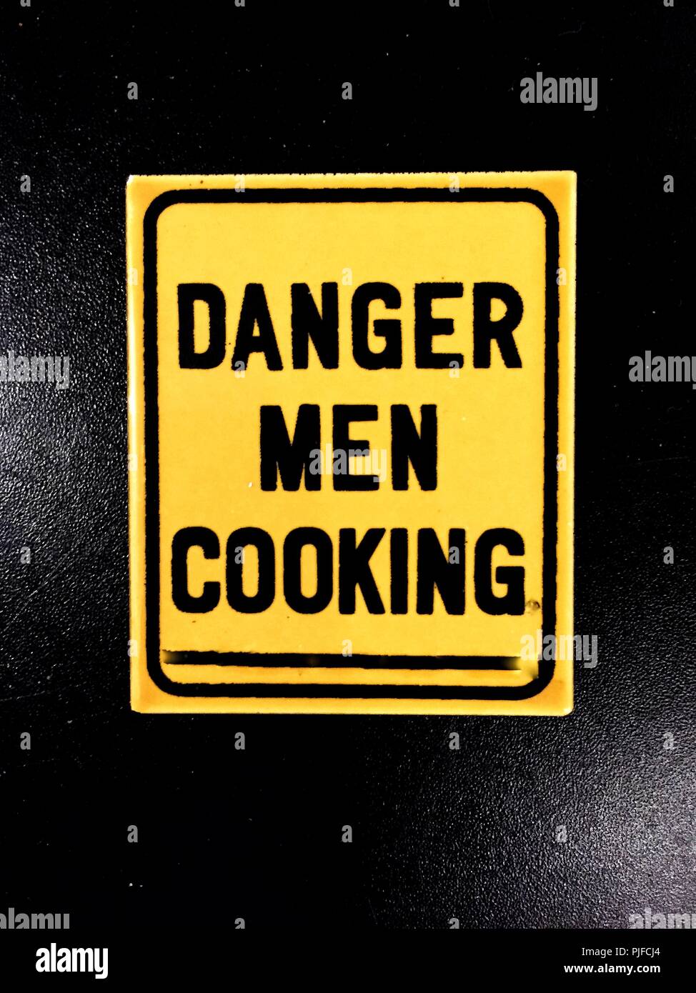 Una divertida nevera imán con las palabras peligro hombres cocinar impreso en Foto de stock