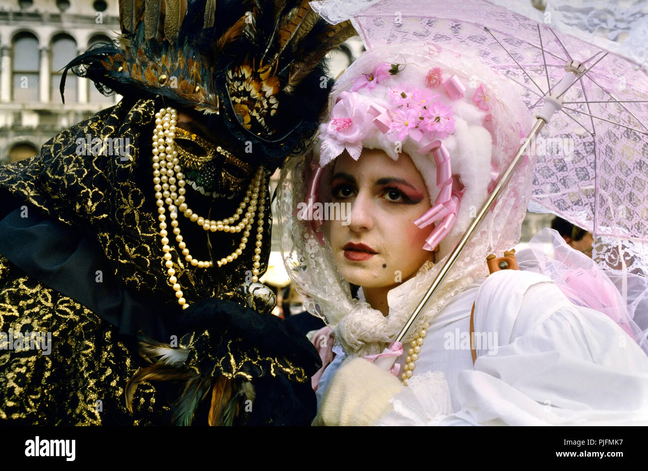 Europa, Italia, una pareja con la máscara en el Carnaval de Venecia. Un  hombre enmascarado con un lobo de oro y perlas. Una mujer vestida de blanco  portando un paraguas rosa Fotografía