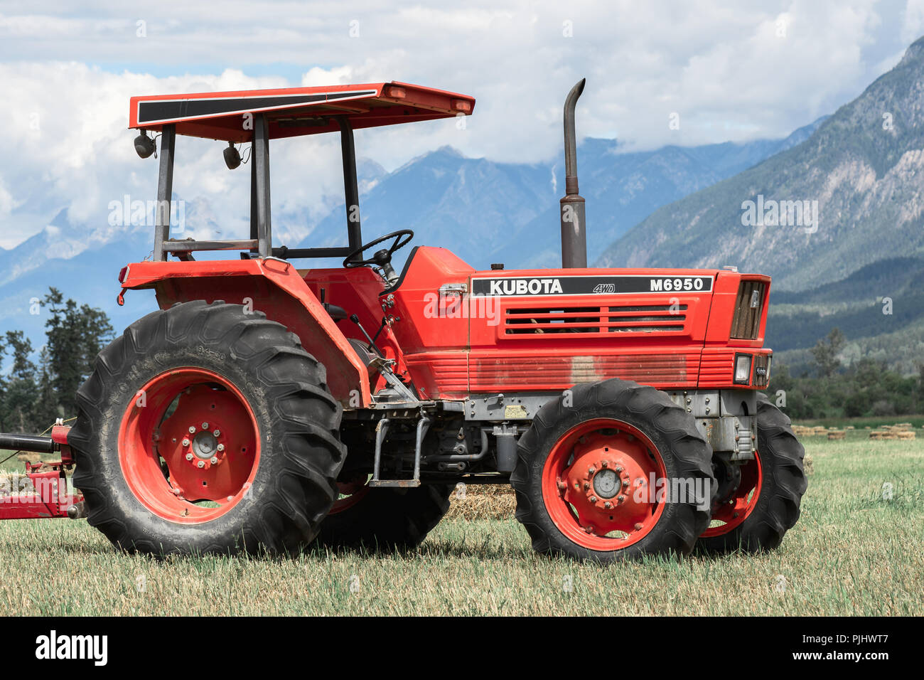 Brisco,BC / Canadá - 11 de julio de 2018:Granja tractor en un campo de heno en las Rocosas Canadienses. Foto de stock