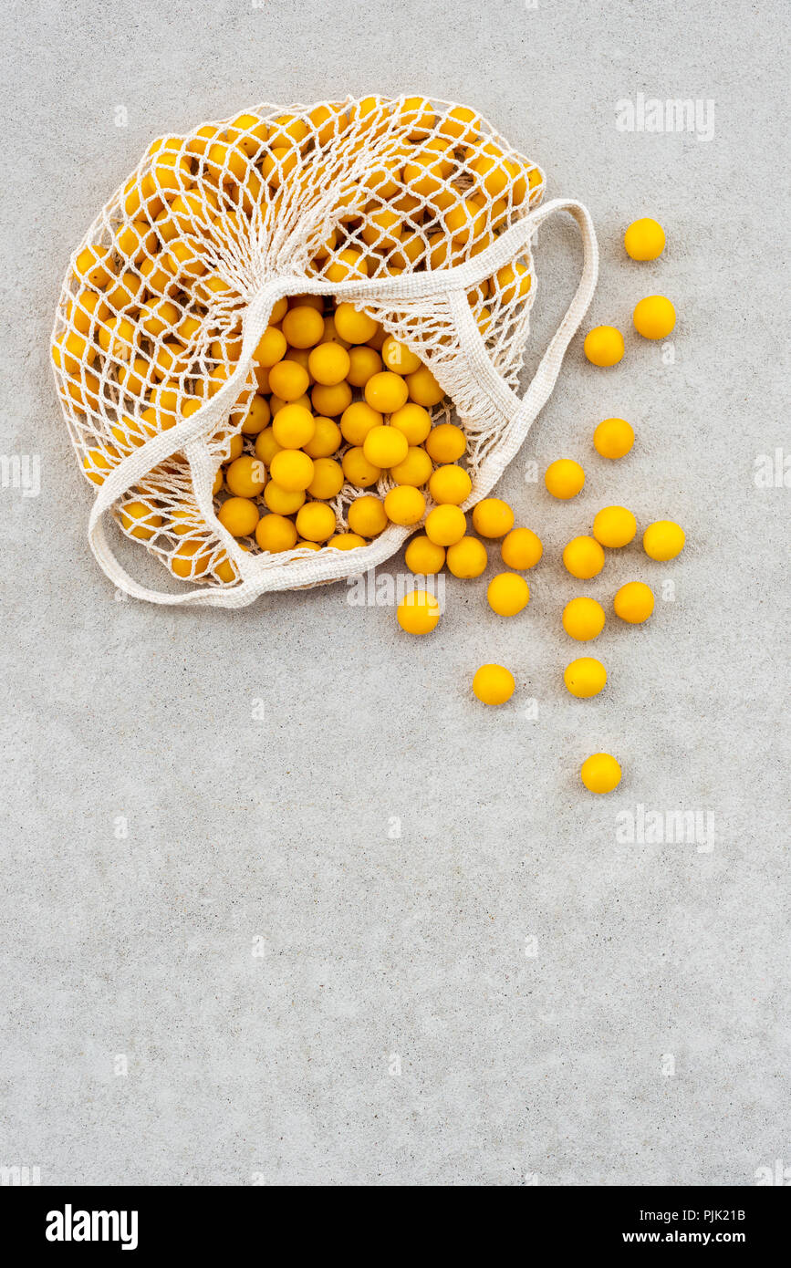 Ciruela amarilla en una bolsa de malla de algodón, sobre fondo de hormigón con espacio de copia. Foto de stock