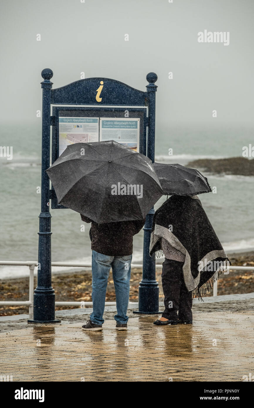 Gales Aberystwyth UK, el sábado 08 de septiembre de 2018 el clima del Reino Unido: La gente caminando bajo su paraguas y envuelto en contra de los elementos de un gris húmedo y triste por la mañana en la playa en Aberystwyth, en Cardigan Bay costa oeste de Gales Foto © Keith Morris / Alamy Live News Foto de stock