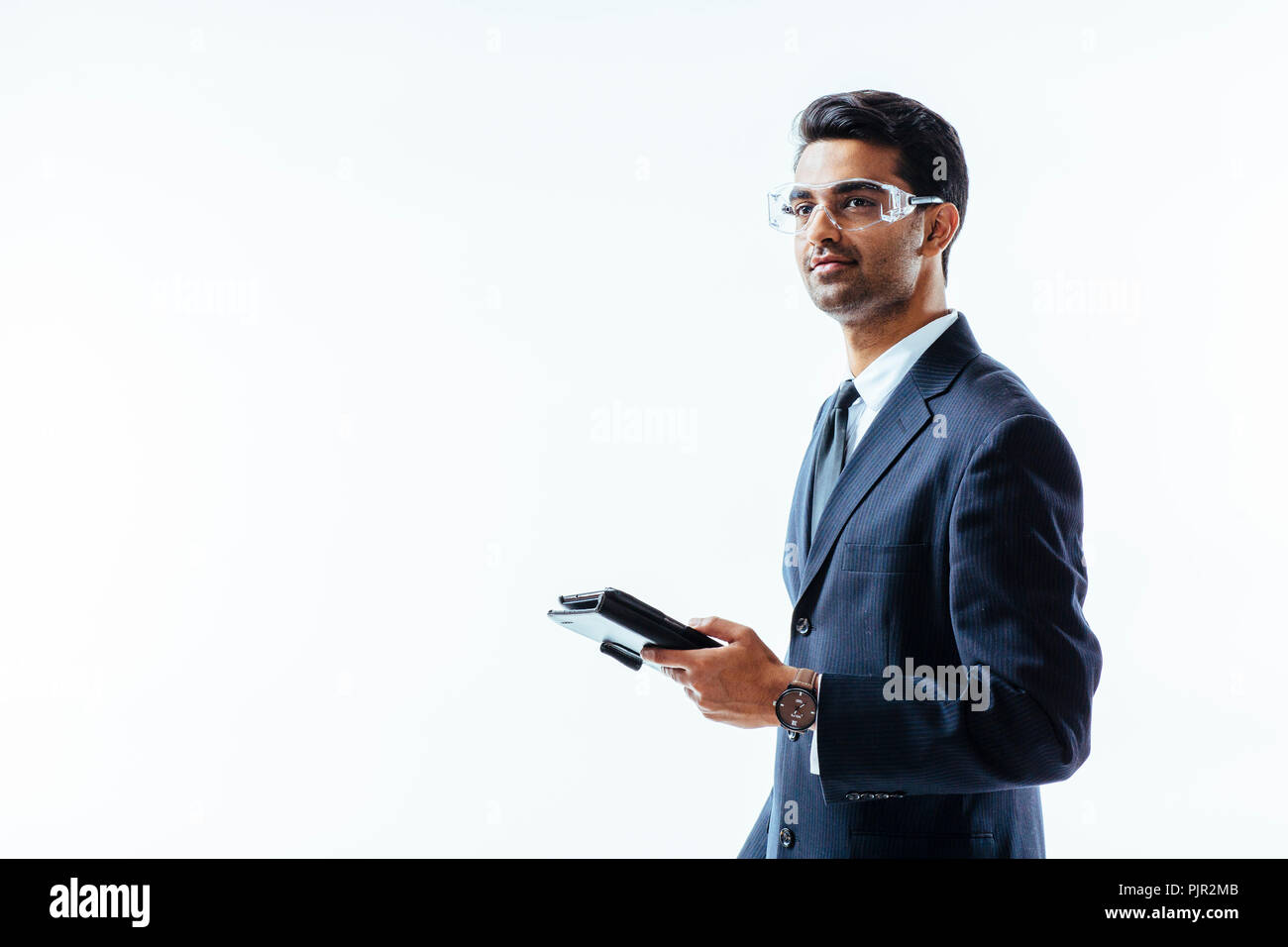 Retrato del hombre en traje de negocios la celebración de tableta electrónica pad y gafas protectoras mirando hacia arriba, aislado sobre fondo blanco studio Foto de stock