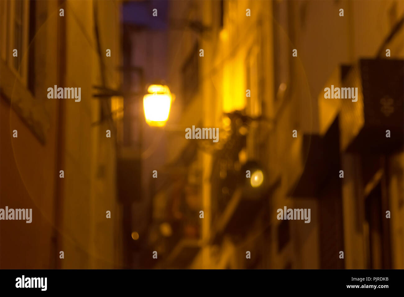 Fondo difuminado. La linterna brilla por la noche, en una pequeña calle en el viejo barrio de Alfama. Lisboa, Portugal. Foto de stock