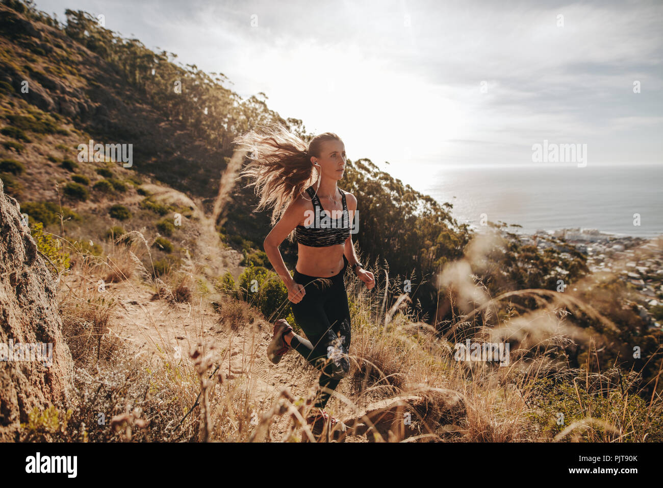 mujer deportiva de entrenamiento para cross country run sobre el sendero de montaña. Hembra corriendo sobre un sendero rocoso en la ladera. Foto de stock