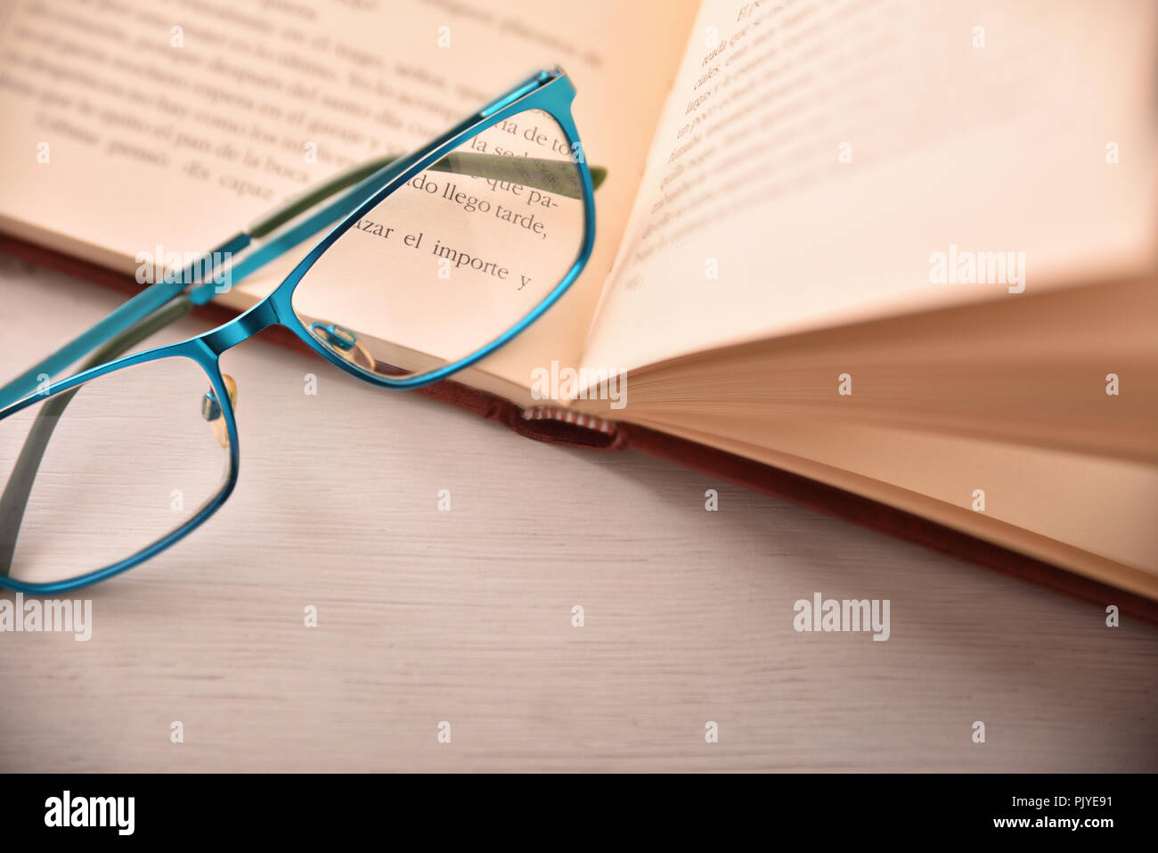Detalle de anteojos en libro abierto sobre la mesa blanca .Concepto necesitan anteojos para leer. Vista desde arriba. Composición horizontal Foto de stock
