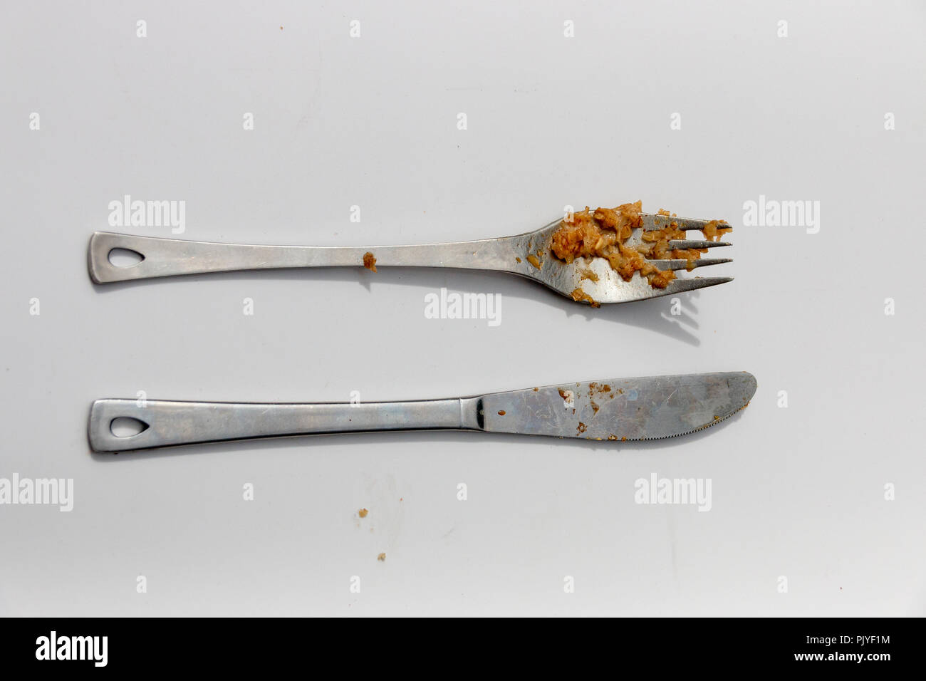 Una vista de cerca de cuchillo y tenedor de plata adirty uno junto al otro en un fondo blanco aislado Foto de stock