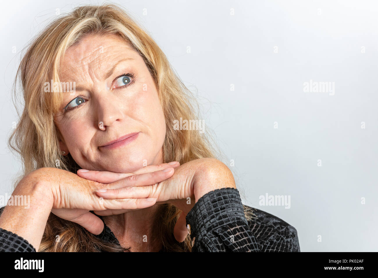 Retrato de estudio de headshot reflexiva atractiva mujer rubia de mediana edad en su cuarenta buscando inquisitivo o cuestionamiento Foto de stock