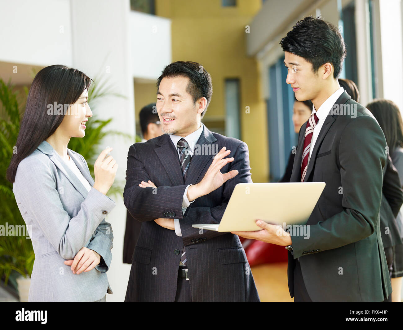 Dos hombres de negocios asiáticos y una empresaria hablando de negocios con ordenador portátil en el vestíbulo de la empresa. Foto de stock