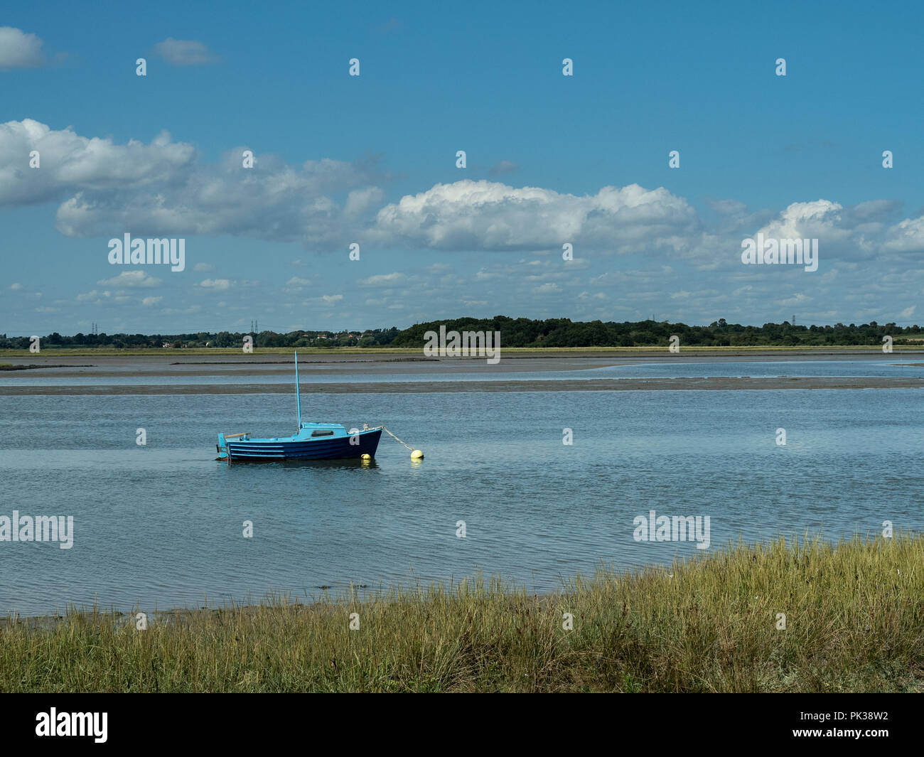 Un tranquilo día en el río Alde en Iken azul incluyendo un barco anclado en el río Foto de stock