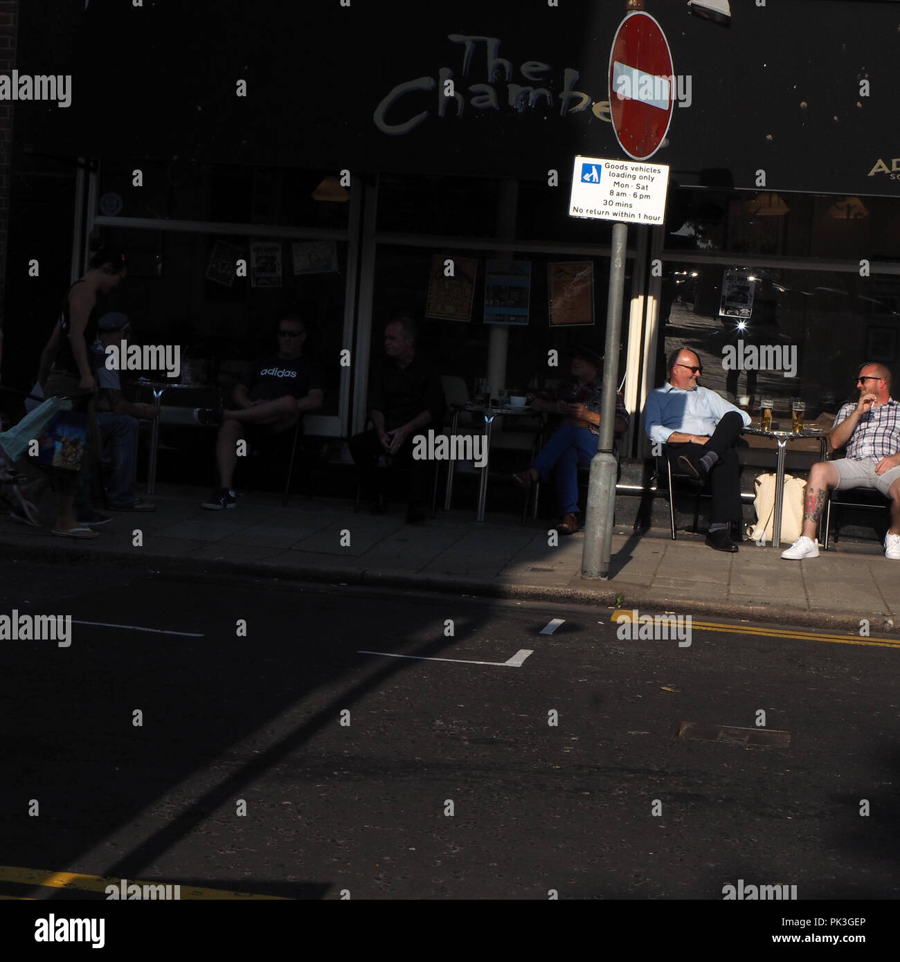 Dos hombres tomando una cerveza al aire libre en una cafetería bajo el sol Foto de stock