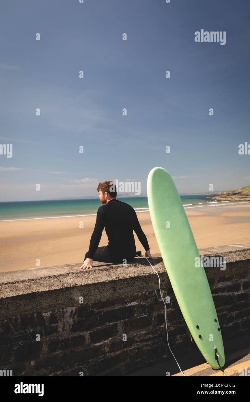 Surfer con surfboard sentado en muro circundante Foto de stock