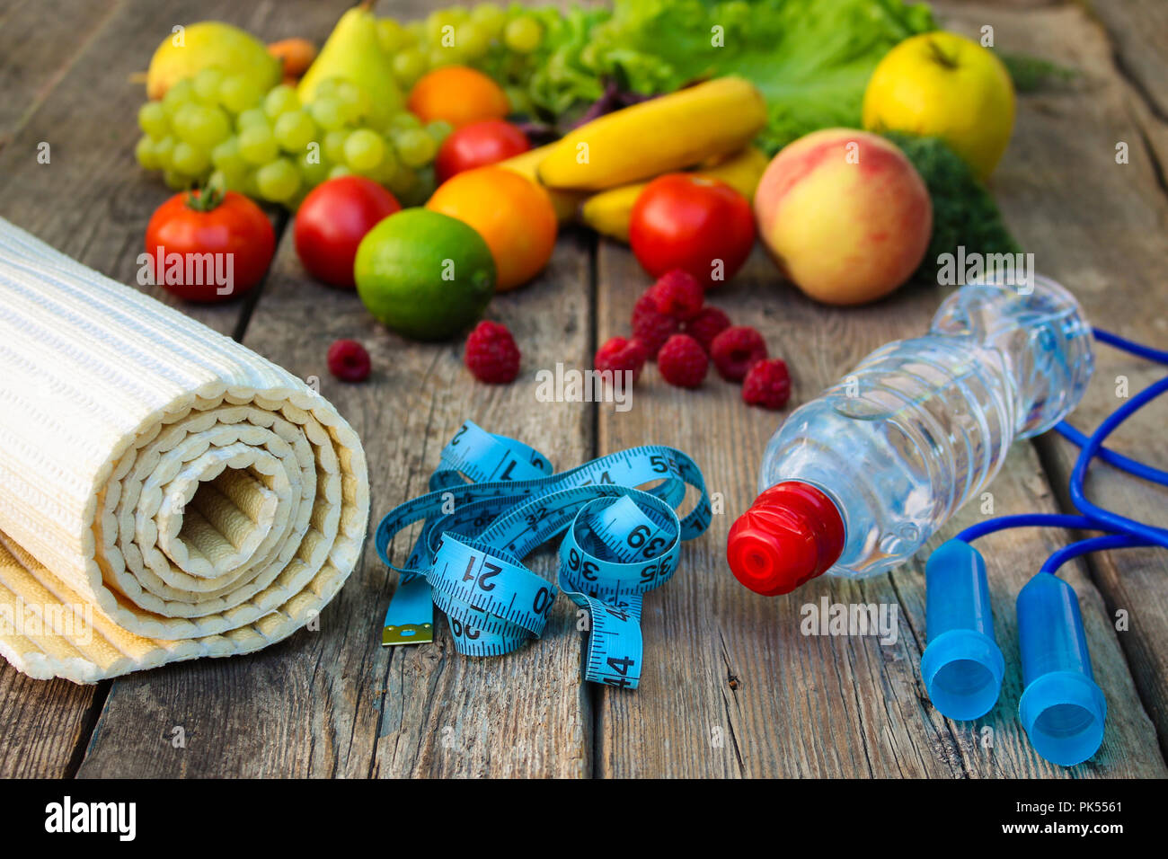 Las frutas, las verduras, el agua, la cinta de medición y artículos deportivos sobre fondo de madera. Foto de stock