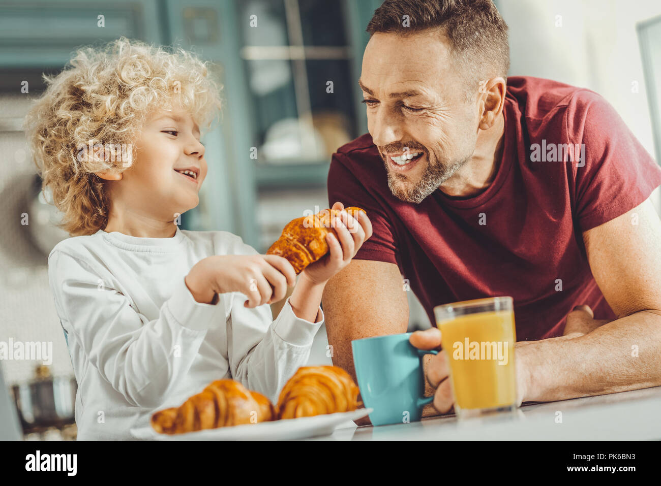 Padre e hijo felices comiendo deliciosos croissants para el desayuno Foto de stock