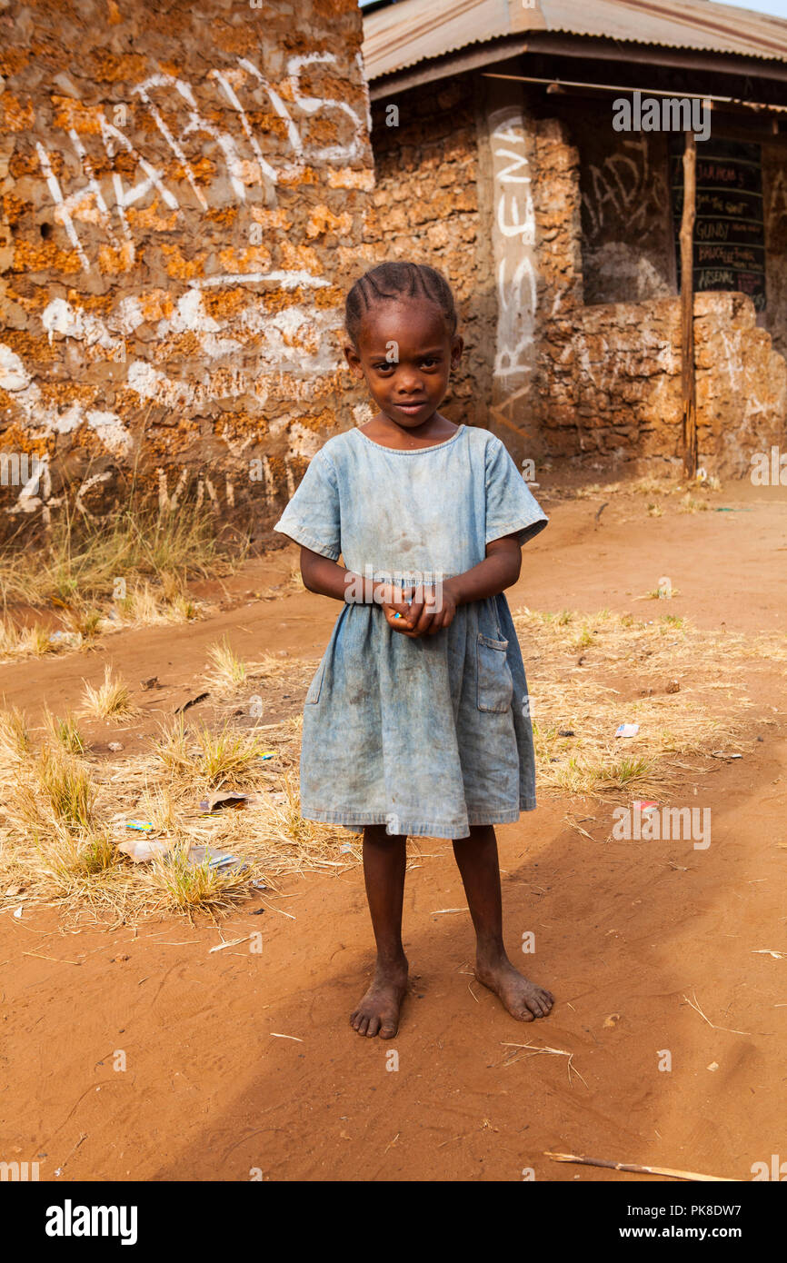ALU - KINONDO, Kenia - Marzo 01, 2018: pequeña y hermosa niña keniana está de pie delante de su casa y mirando a la cámara Foto de stock
