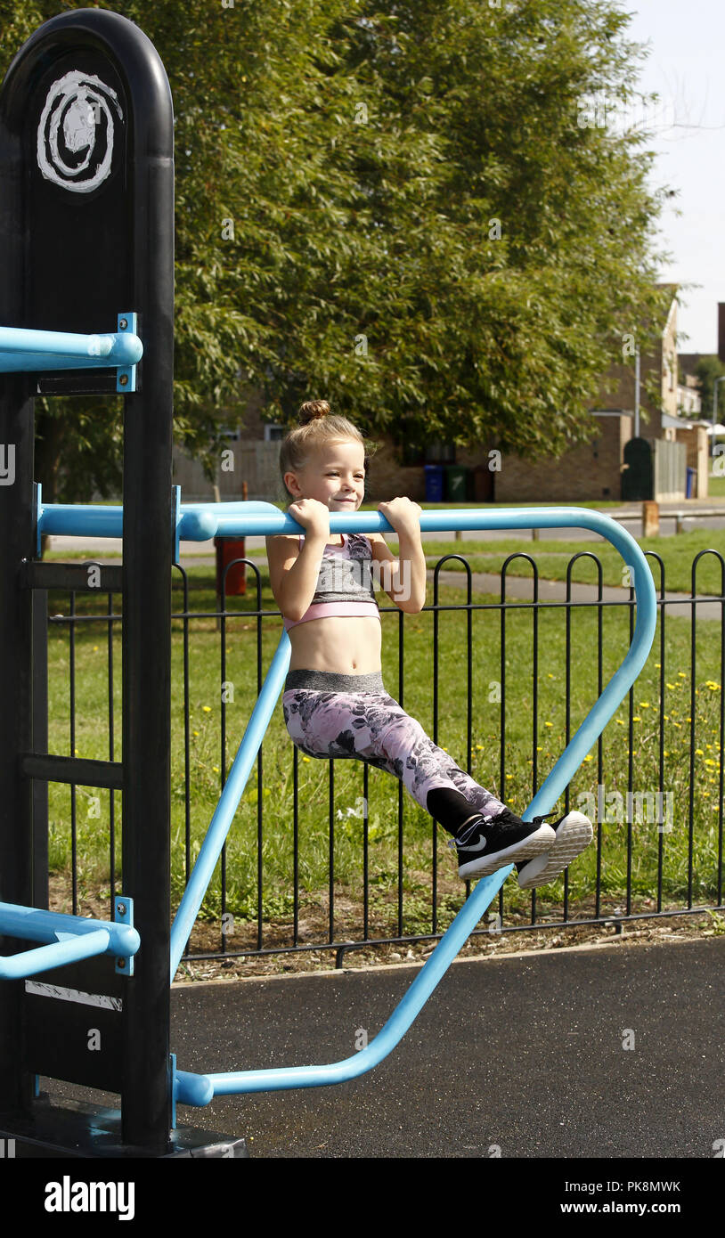 Una niña de seis años haciendo 'pull ups" en el libre uso de los equipos en un área de gimnasio al aire libre Foto de stock