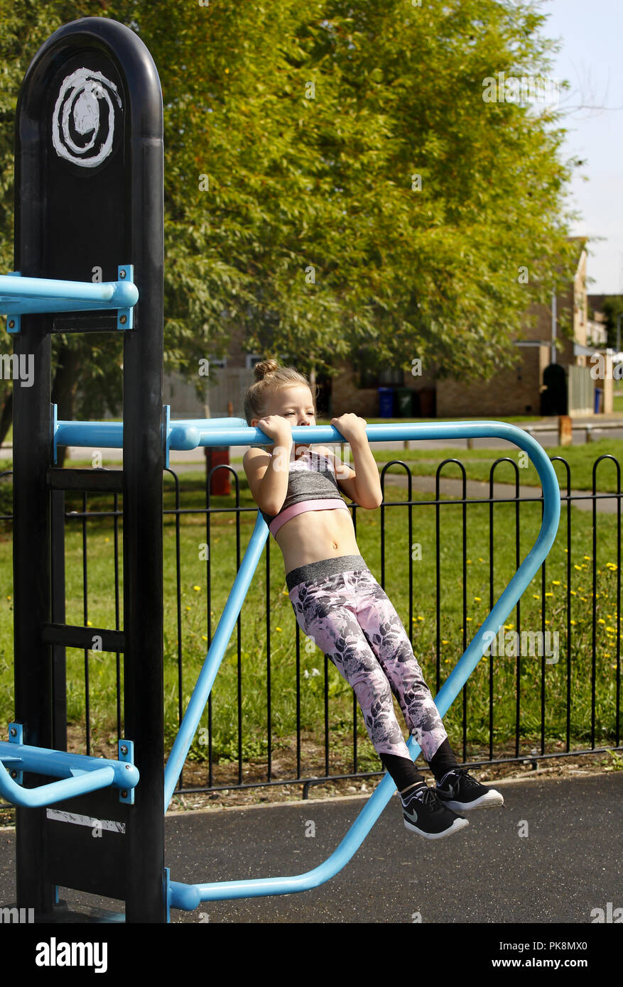 Una niña de seis años haciendo el "tirar ups', el equipamiento en un libre para utilizar un área de ejercicios al aire libre Foto de stock