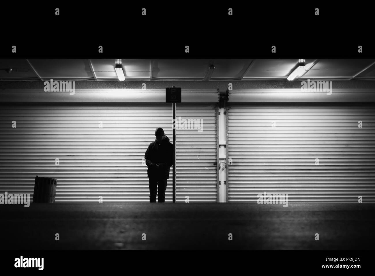 Un hombre esperando en una parada de autobús en la noche delante de las puertas de seguridad del rodillo en Nueva Zelanda Foto de stock