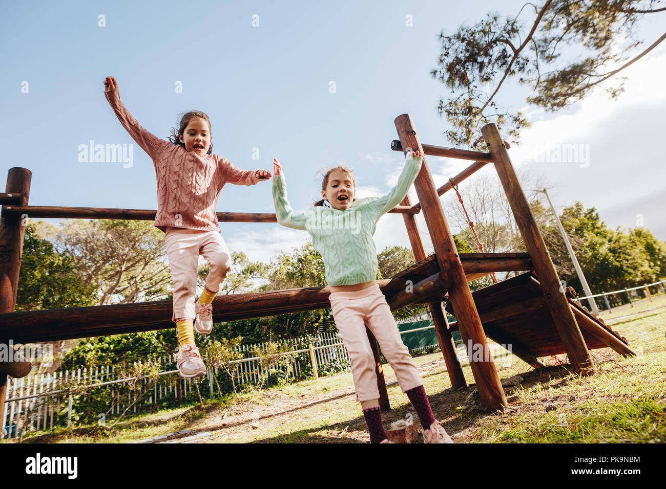 Poco feliz hermanas gemelas saltando de un registro de madera en el parque poco chicas que se divierten en la piscina infantil. Foto de stock