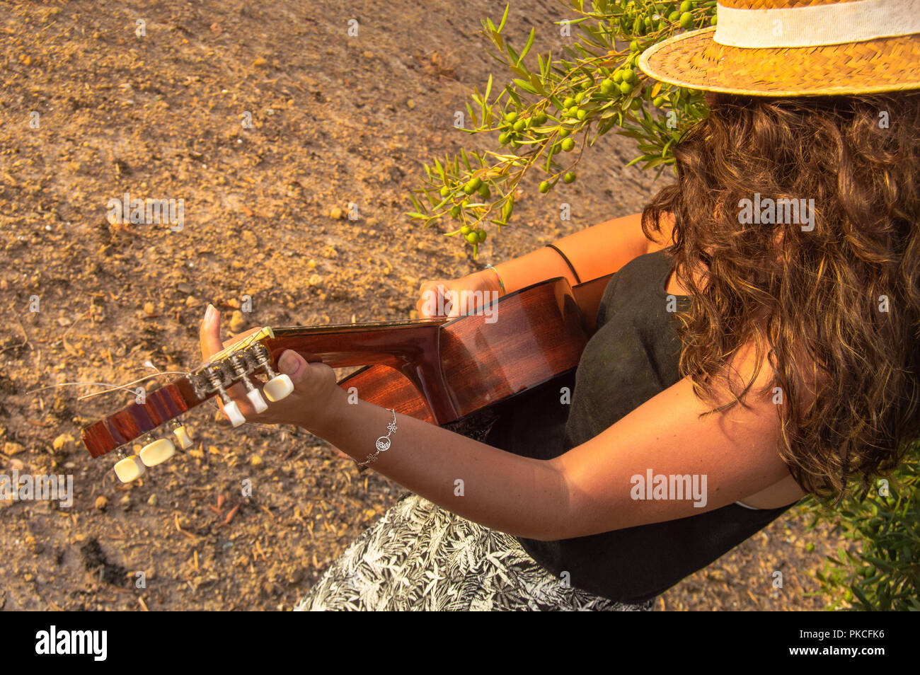 Mujer joven con sombrero de paja de pie y tocando una guitarra clásica  española o en un paisaje andaluz de olivos al atardecer Fotografía de stock  - Alamy