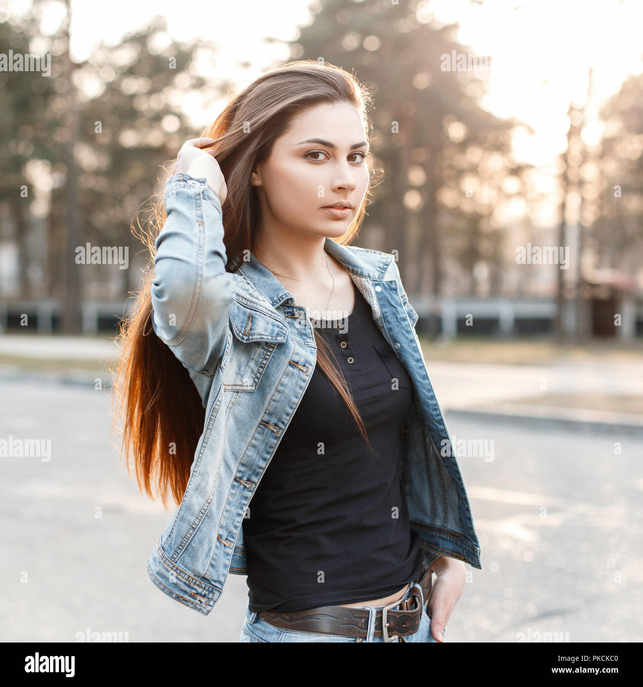 Elegante joven en jeans de moda ropa corrige su largo cabello al atardecer  Fotografía de stock - Alamy