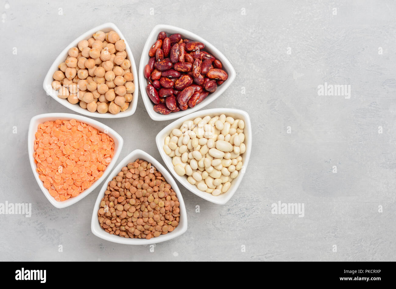 Selección de legumbres secas, lentejas y guisantes en cuencos blancos sobre fondo de cemento gris. Foto de stock