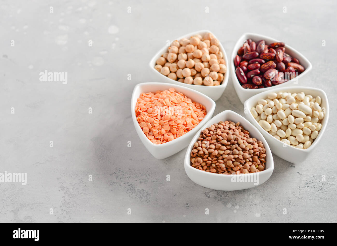 Selección de legumbres secas, lentejas y guisantes en cuencos blancos sobre fondo de cemento gris. Foto de stock