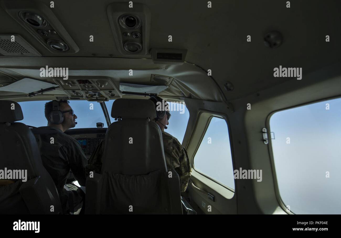 KABUL, Afganistán (25 de julio, 2018) -- un piloto de la Fuerza Aérea Afgana (izquierda) de un Cessna 208B asignada a la 1ª Ala de la fuerza aérea afgana y un piloto estadounidense (derecha) asignado a la 438th ala expedicionaria aérea como parte de capacitar, asesorar y ayudar Command-Air (TAAC-aire) en el Aeropuerto Internacional de Hamid Karzai (HKIA), Afganistán, mire el paisaje durante un vuelo de entrenamiento el 25 de julio de 2018. La misión de capacitar, asesorar y ayudar Command-Air es capacitar, asesorar y ayudar a la Defensa Nacional Afgano y las fuerzas de seguridad para el desarrollo profesional, capaz y sostenibles de la Fuerza Aérea. Foto de stock