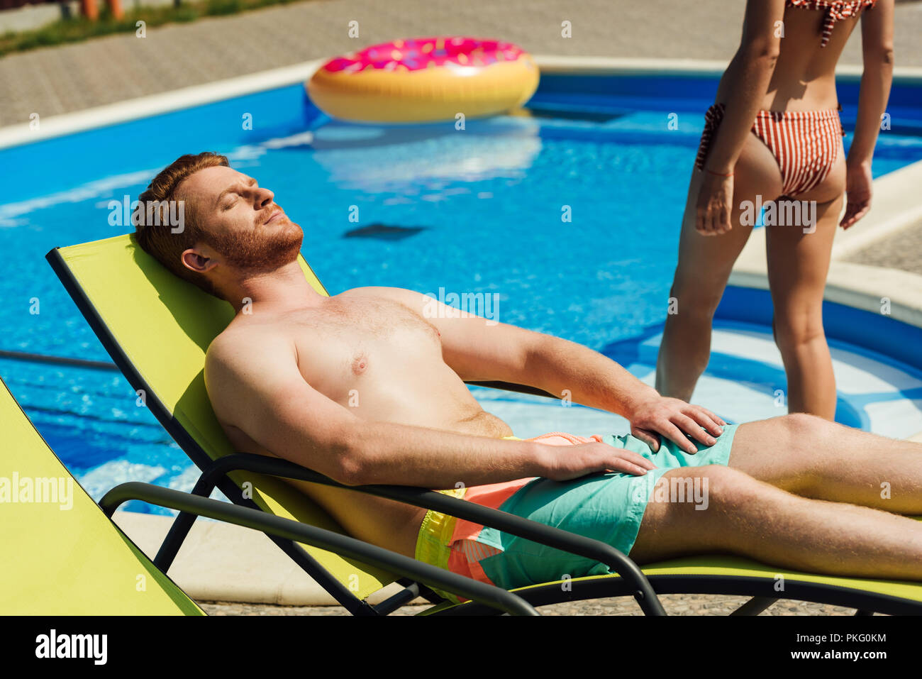 Apuesto joven bronceado en las hamacas mientras su novia entrando en la  piscina Fotografía de stock - Alamy