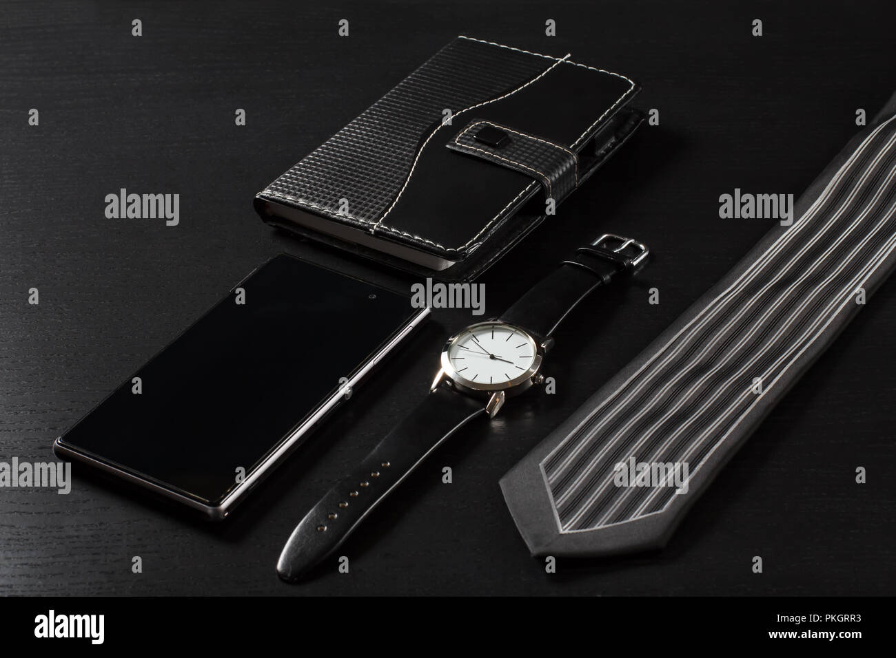 Reloj con una correa de cuero, portátil en funda de cuero, vender el  teléfono, corbata de seda sobre un fondo negro Fotografía de stock - Alamy