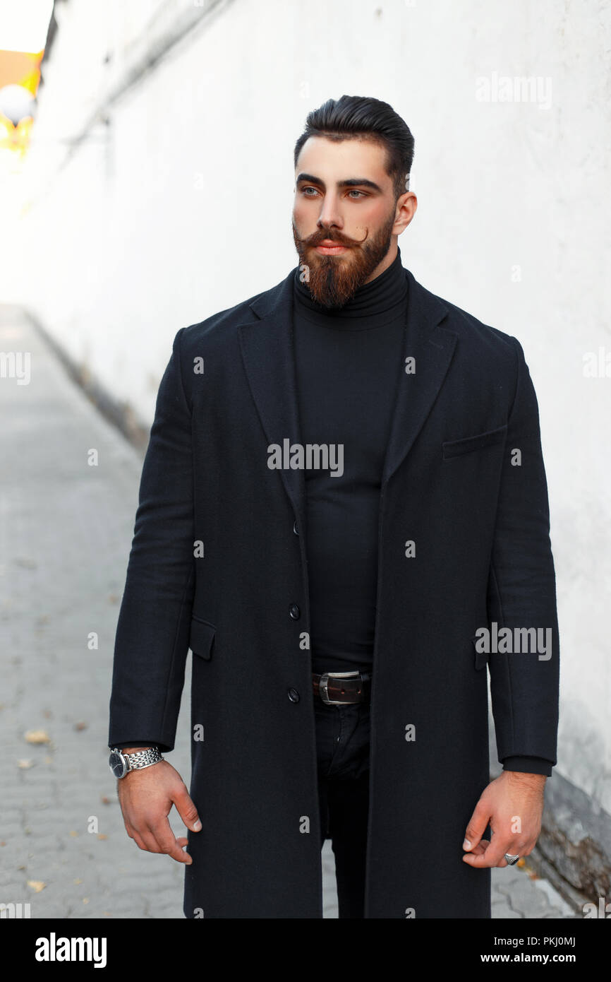 Apuesto joven hipster hombre con cabello y barba negra en ropa de moda con  el escudo en la calle Fotografía de stock - Alamy