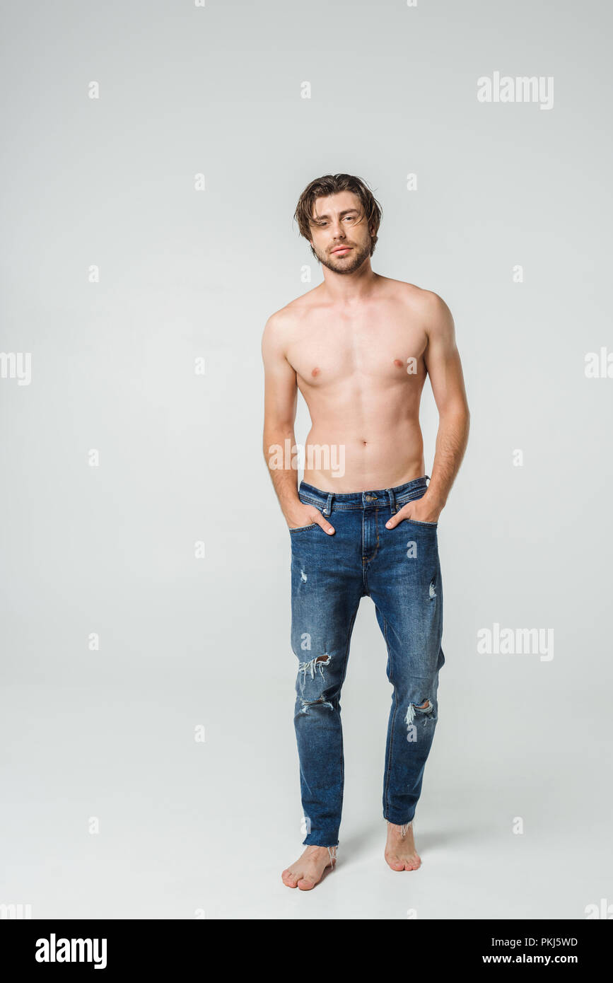 Los jóvenes descamisados hombre en jeans con las manos en los bolsillos  posando sobre fondo gris Fotografía de stock - Alamy