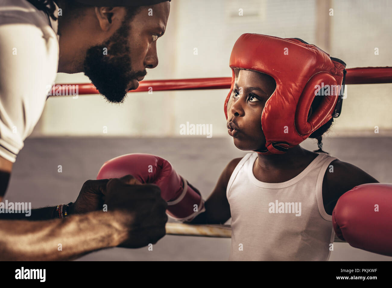 Entrenador de boxeo dando instrucciones a un niño antes de una pelea. Cabrito en guantes de boxeo y tocado escuchar a su entrenador. Foto de stock