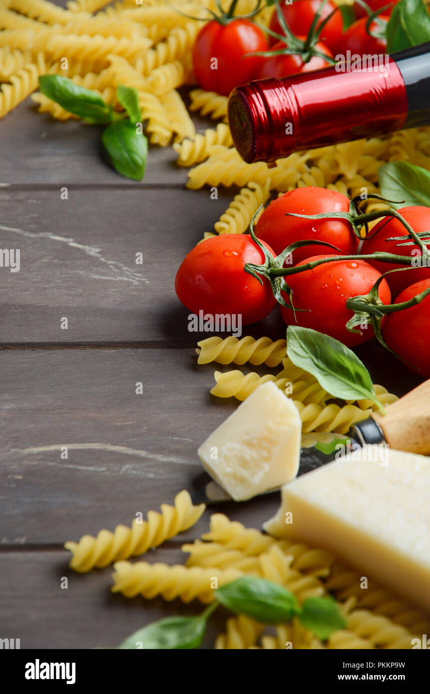 Comida italiana - materias fusilli, tomate, albahaca y vino en la mesa de madera. Foto de stock