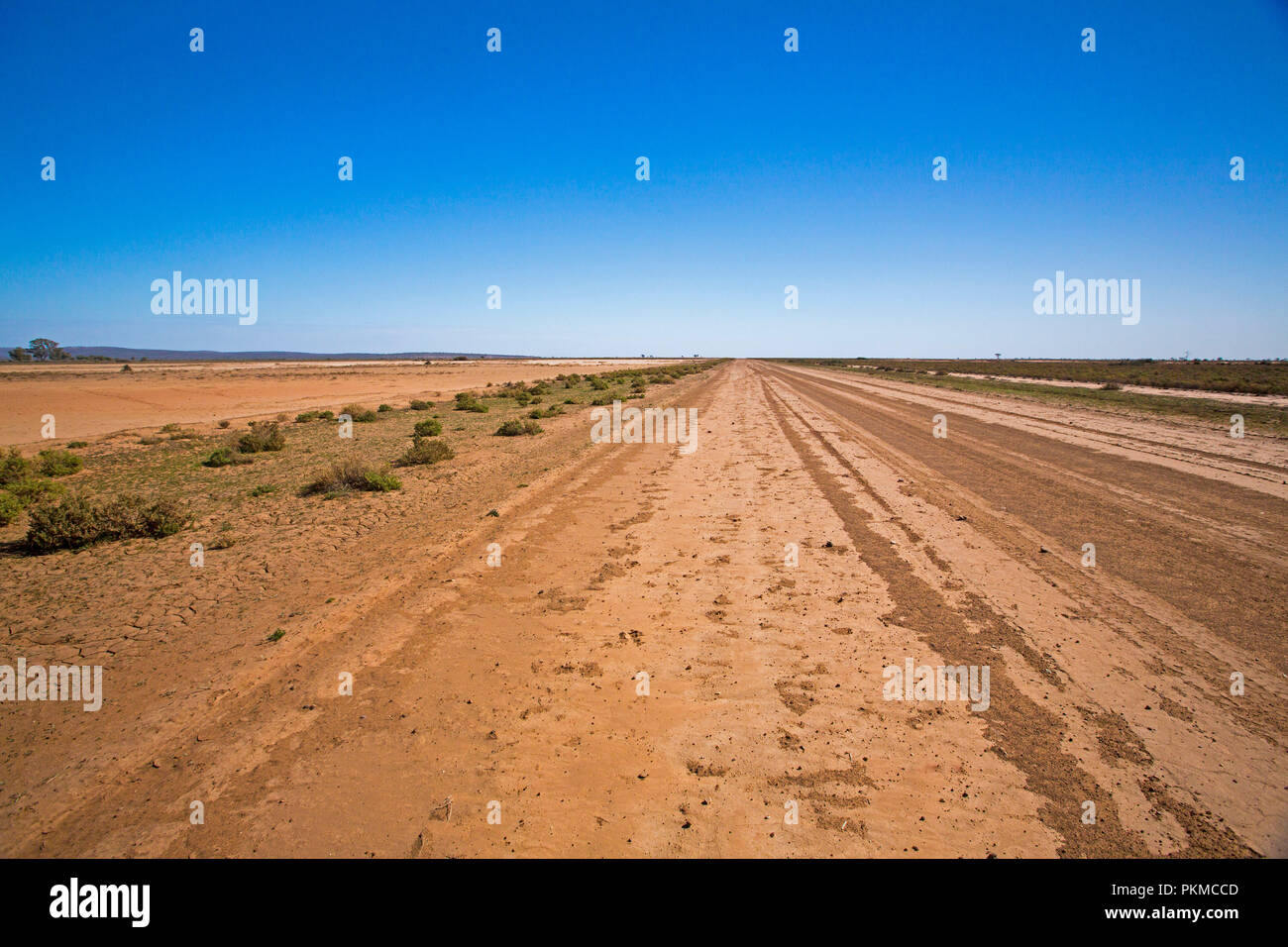 Largo camino del desierto australiano cortar a través de árido paisaje desprovisto de vegetación durante la sequía y estiramiento para lejano horizonte bajo un cielo azul Foto de stock
