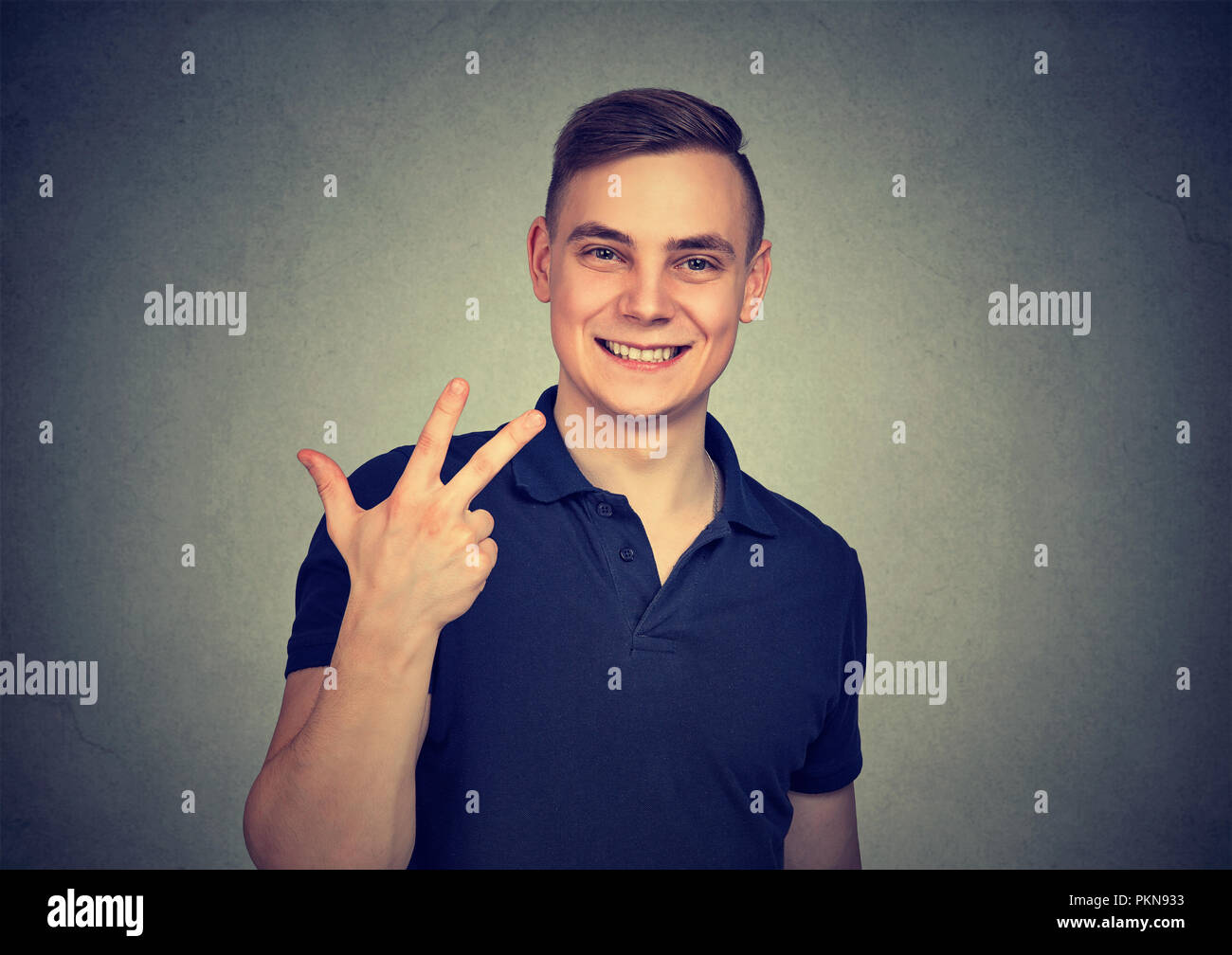 Joven mostrando tres dedos mientras ofrece ocuparse y sonriendo a la cámara sobre fondo gris Foto de stock