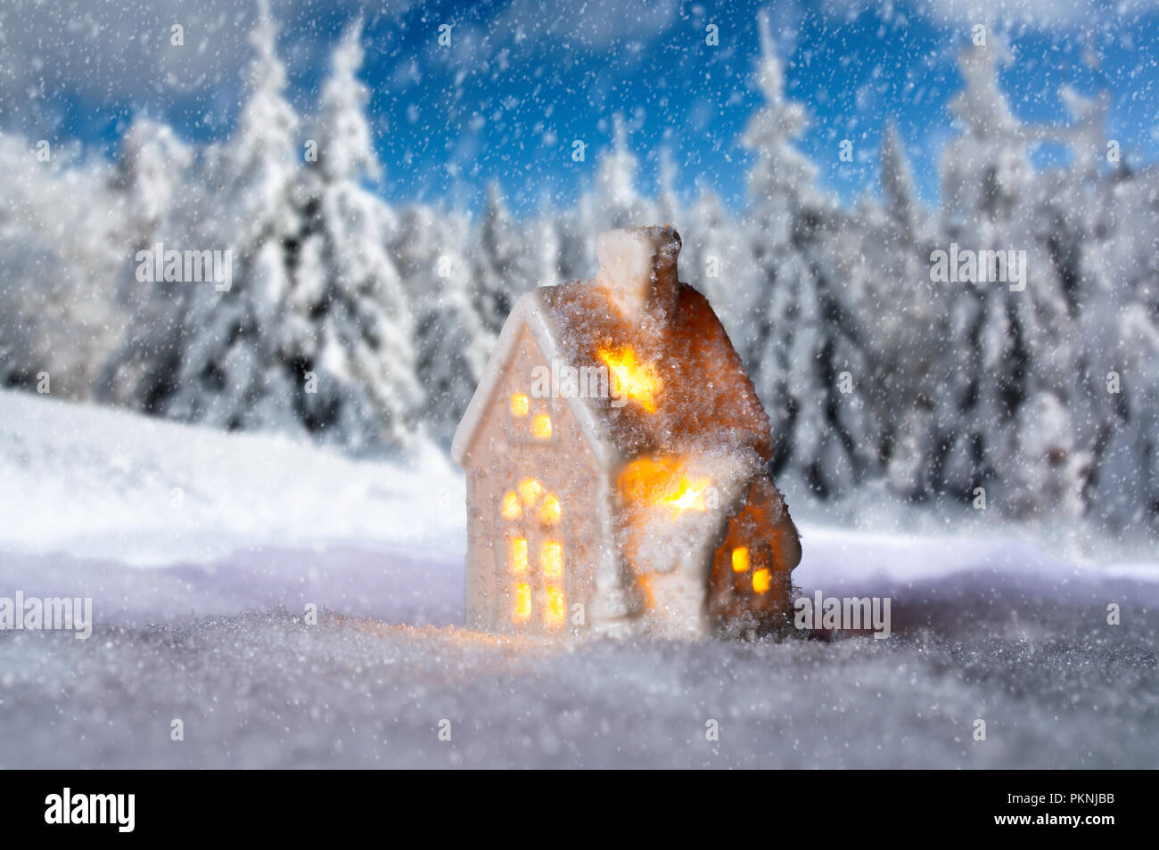Pequeña casa con luces delante del paisaje nevado de invierno Foto de stock
