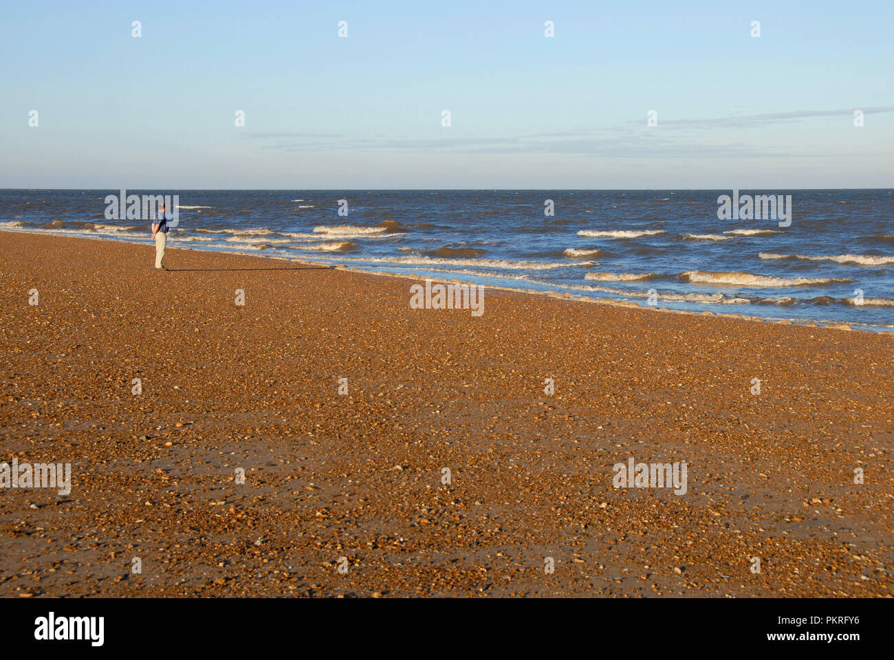 Hombre solitario en la orilla del mar mirando las olas rompen, temprano en la mañana, Hunstanton, Norfolk, Inglaterra Foto de stock