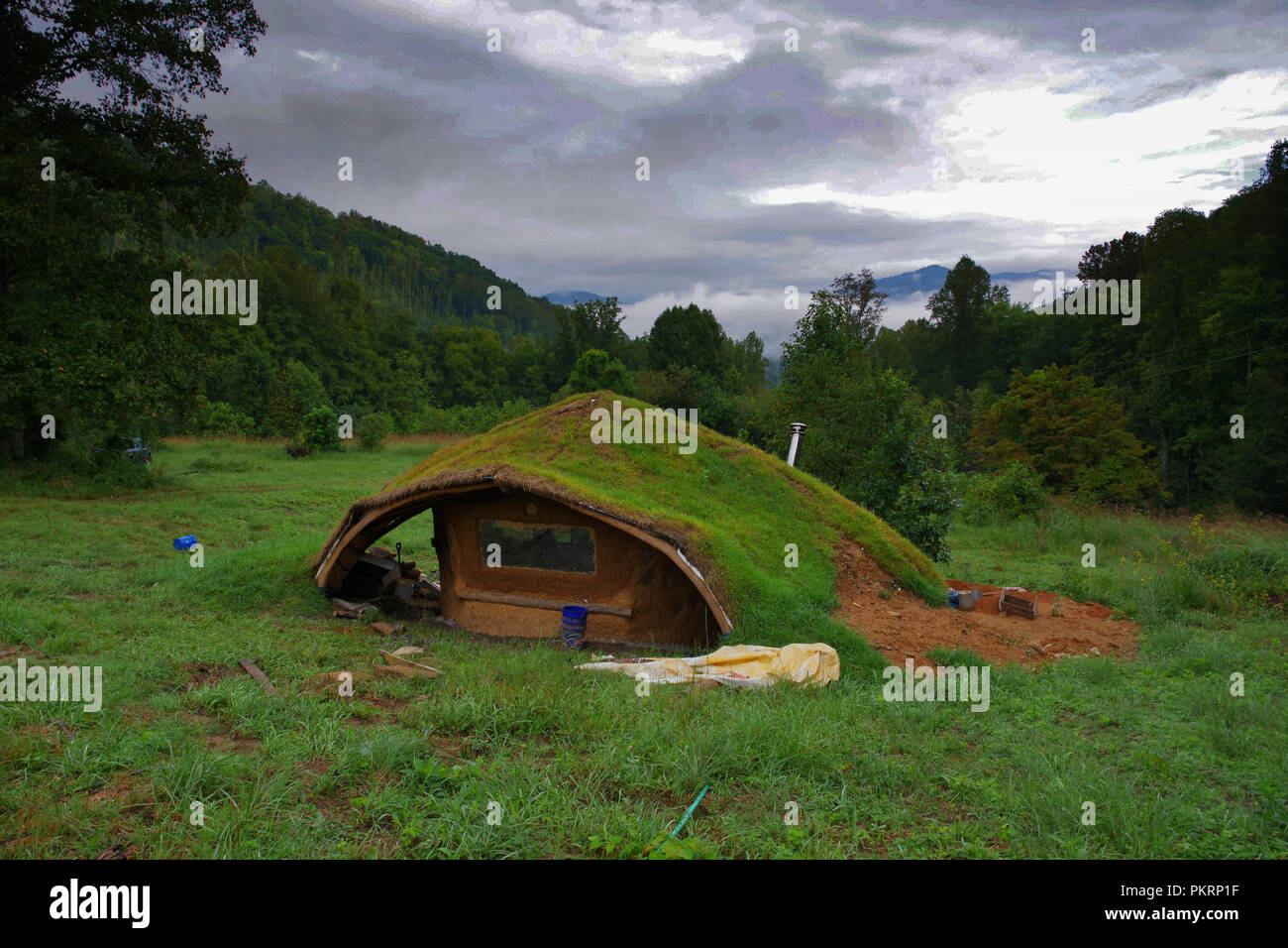 Hobbit house en las brumosas montañas. Pequeña casa de barro cubierto de hierba y musgo. La arquitectura sostenible. Foto de stock