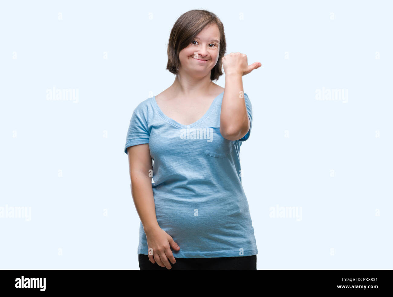 Mujer adulta joven con síndrome de down más antecedentes aislados sonriendo con cara feliz mirando y señalando al lado con el dedo pulgar hacia arriba. Foto de stock