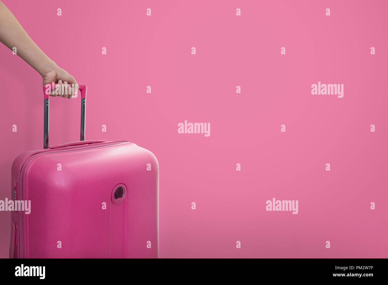 Mano sujetando traveler pink maleta o equipaje de tamaño de cabina sobre  fondo de color rosa con espacio de copia, el viaje y el concepto de viaje  Fotografía de stock - Alamy