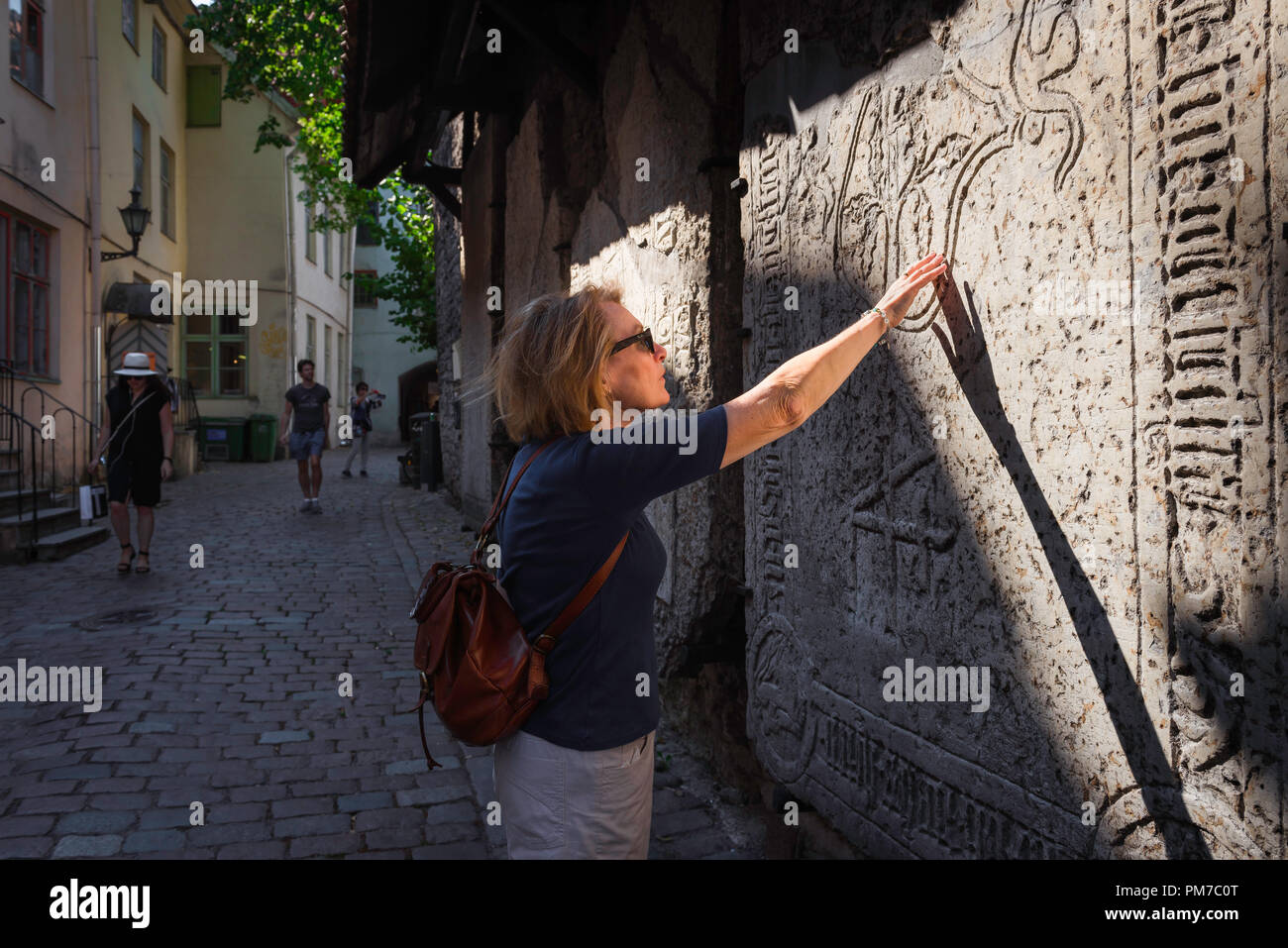 Mujer viaje explorar, vista de una mujer adulta viajero tocando una lápida medieval en el casco antiguo histórico (Vanalinn) de la zona de Tallin, Estonia. Foto de stock