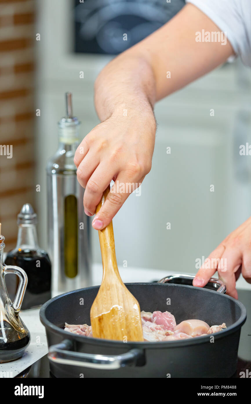 Hombre cocina la carne en una sartén. Mano con espátula para remover rojo y  blanco sartén llena de carne Fotografía de stock - Alamy