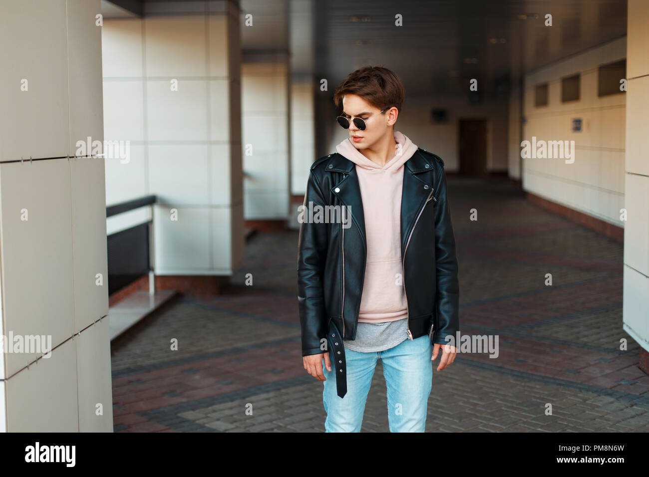 Apuesto joven aviador gafas de sol en la chaqueta de cuero negro y rosa  sudadera posando cerca del edificio Fotografía de stock - Alamy