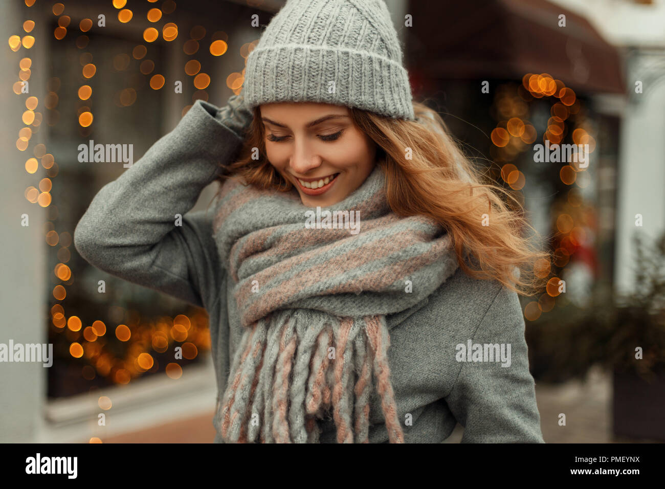 Moda hermosa niña alegre en estilo vintage Chaqueta con tejido gorro con  bufanda de moda cerca de luces amarillas en la calle Fotografía de stock -  Alamy