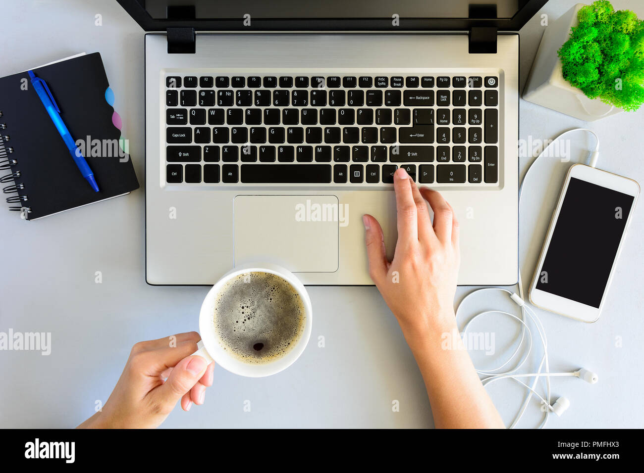 Oficina de madera gris escritorio con ordenador portátil,  smartphone,cuaderno, pluma y una taza de café. Manos femeninas, utilizando  un ordenador portátil y sosteniendo una taza de café Fotografía de stock -  Alamy